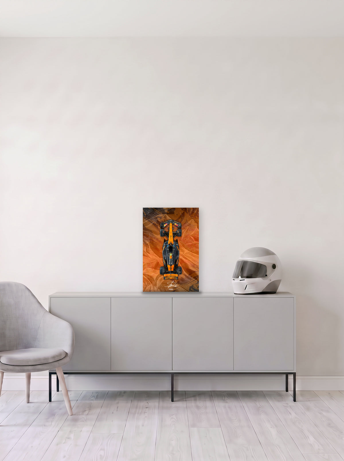Poster del McLaren de Lando Norris sobre fondo naranja satinado, en medida 33,3 x 50 cm, apoyado sobre un aparador gris junto a un casco de competicion, decoracion racing de MOA-Grafics.