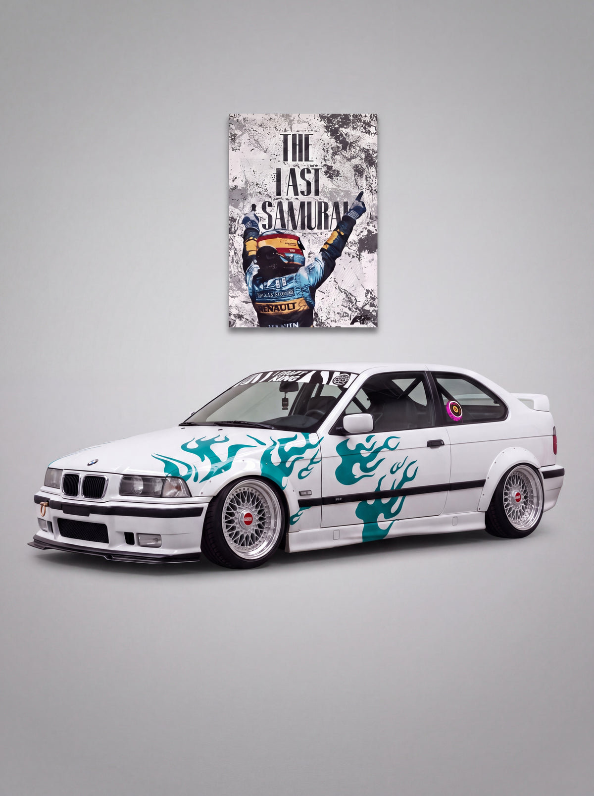 Un BMW Serie 3 Compact blanco con llamas turquesa en el lateral, bajo un póster enmarcado colgado en la pared