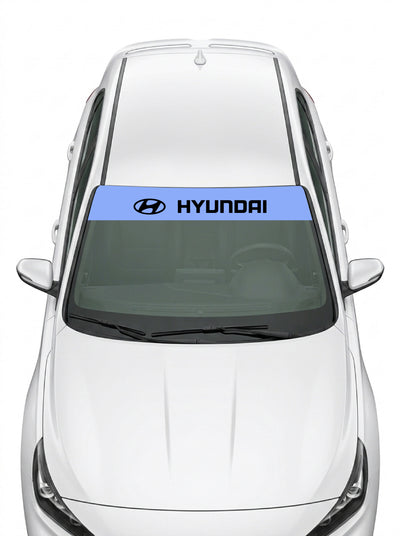 Parasol de vinilo Hyundai azul con el emblema oval y el lettering HYUNDAI en negro, instalado en el parabrisas de un Hyundai blanco