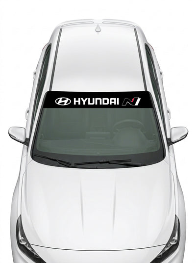 Parasol de vinilo Hyundai N negro con el emblema, el lettering HYUNDAI y el logo N, instalado en el parabrisas de un Hyundai blanco