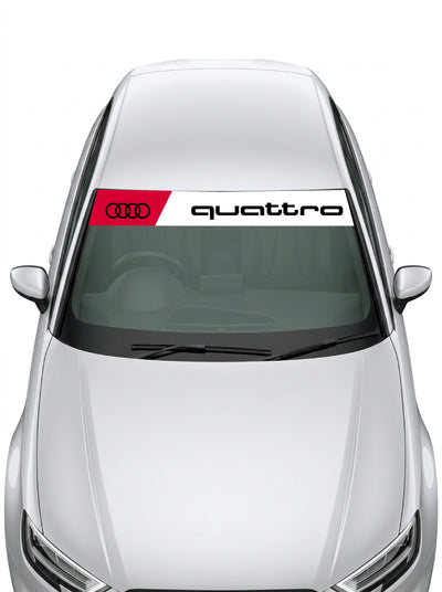 Parasol de vinilo Audi Quattro de 150x25 cm en blanco con recuadro rojo de cuatro anillos y el lettering quattro en negro, instalado en el parabrisas