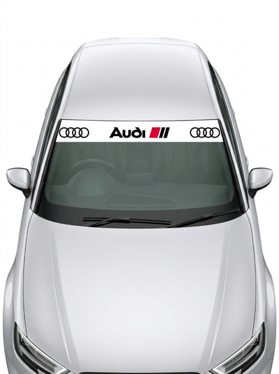 Parasol de vinilo Audi Sport blanco instalado en el parabrisas de un coche: los cuatro anillos a cada extremo y el lettering Audi con las tres barras rojas en el centro, en negro sobre fondo blanco, de MOA-Grafics.