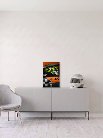 Poster del casco de Lando Norris asomando del cockpit del McLaren, en medida 33,3 x 50 cm, apoyado sobre un aparador gris junto a un casco de competicion, decoracion racing de MOA-Grafics.