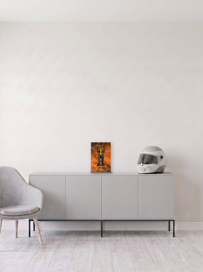 Poster del McLaren de Lando Norris sobre fondo naranja satinado, en medida 20 x 30 cm, apoyado sobre un aparador gris junto a un casco de competicion, decoracion racing de MOA-Grafics.