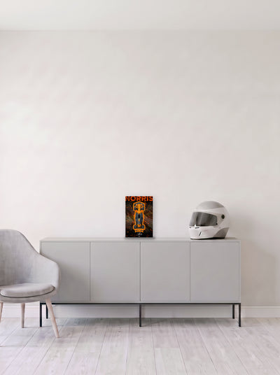 Poster del McLaren de Lando Norris con su apellido en grande y salpicaduras naranjas, en medida 20 x 30 cm, apoyado sobre un aparador gris junto a un casco de competicion, decoracion racing de MOA-Grafics.